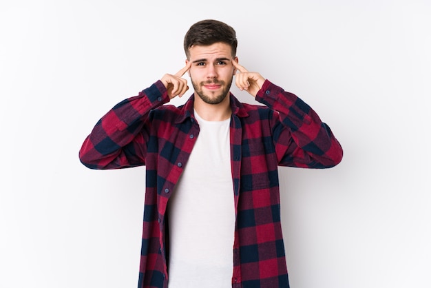 Hombre caucásico joven posando en una pared blanca aislada centrada en una tarea, manteniendo los dedos índice apuntando a la cabeza.