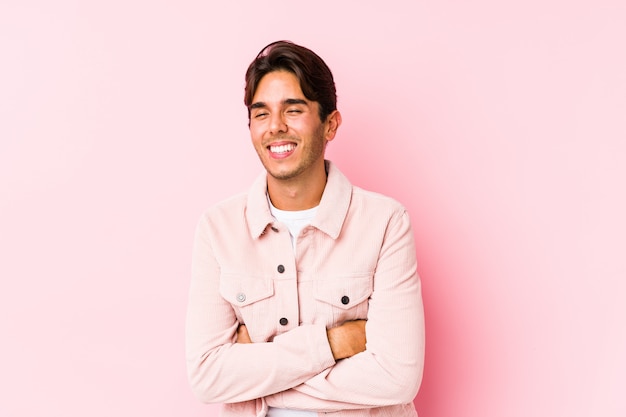 Hombre caucásico joven posando en una pared rosa riendo y divirtiéndose.