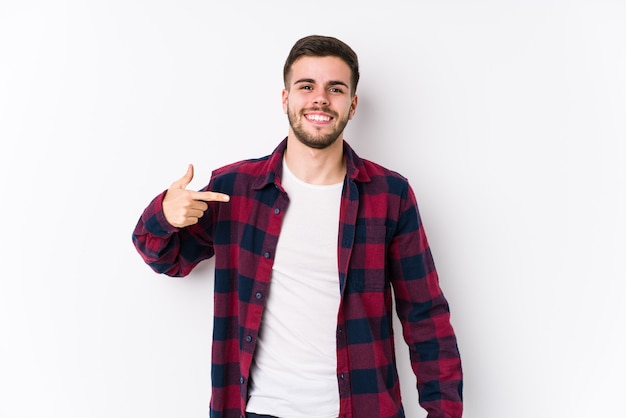 Foto hombre caucásico joven posando en una persona aislada de fondo blanco apuntando con la mano a un espacio de copia de camisa, orgulloso y seguro