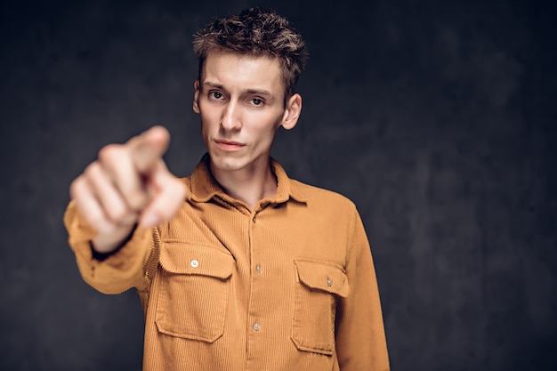 Hombre caucásico joven punto con el dedo sobre fondo gris oscuro