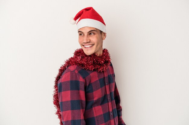 Foto el hombre caucásico joven que celebra la navidad aislado en el fondo blanco mira a un lado sonriente, alegre y agradable.