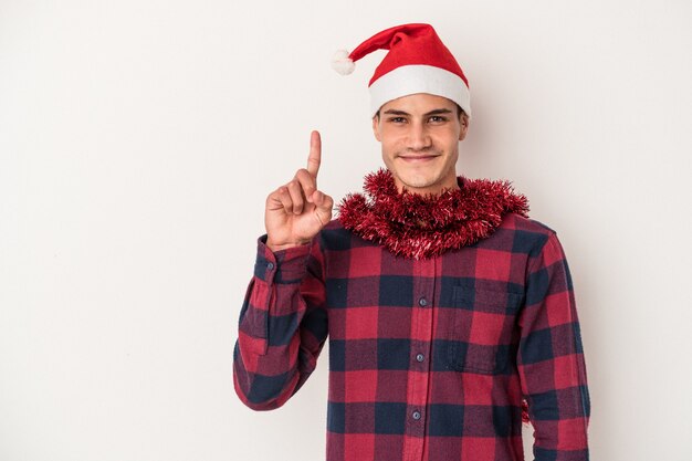 Hombre caucásico joven que celebra la Navidad aislado en el fondo blanco que muestra el número uno con el dedo.