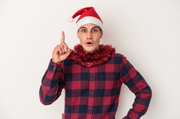 Hombre caucásico joven que celebra la Navidad aislado en el fondo blanco que tiene una idea, concepto de la inspiración.