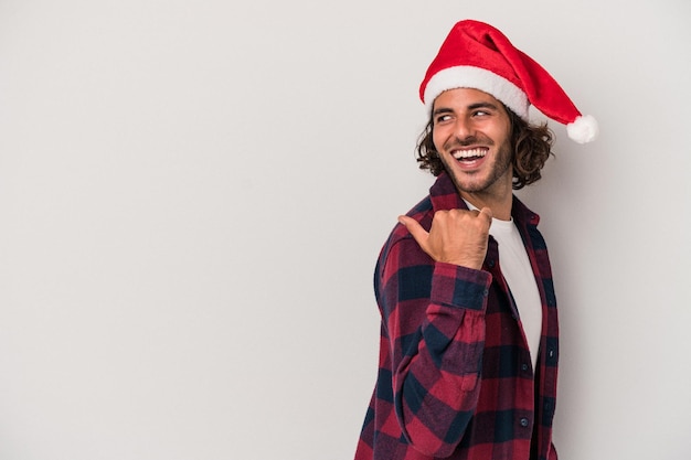 Hombre caucásico joven que celebra la Navidad aislado en puntos de fondo gris con el dedo pulgar lejos, riendo y despreocupado.