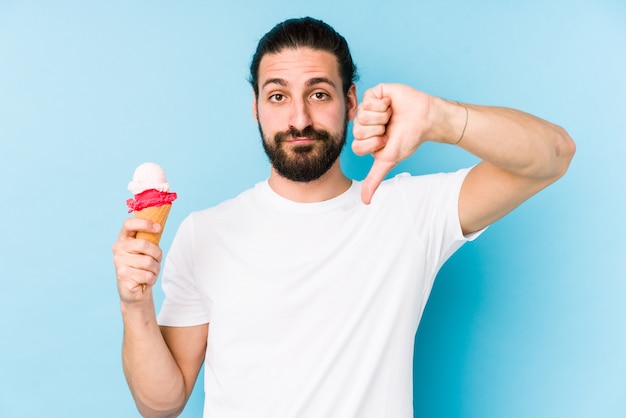 Hombre caucásico joven que come un helado aislado mostrando un gesto de la aversión, pulgares abajo. Concepto de desacuerdo