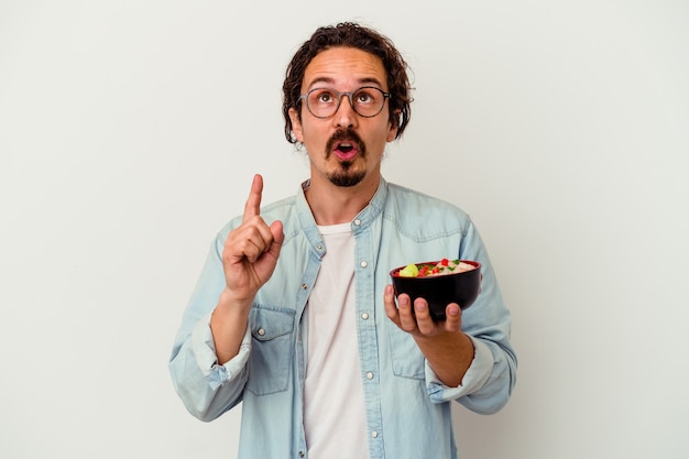 Hombre caucásico joven que come un ramen aislado en blanco apuntando al revés con la boca abierta.