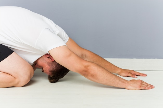 Foto hombre caucásico joven que estira practicando yoga