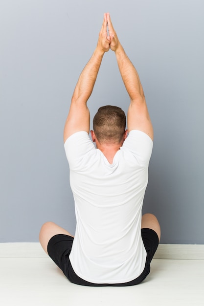 Foto hombre caucásico joven que estira practicando yoga.