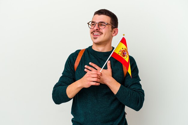 Hombre caucásico joven que estudia inglés aislado en la pared blanca ríe a carcajadas manteniendo la mano en el pecho.