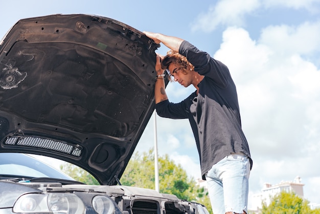 Hombre caucásico joven que intenta reparar una avería en su coche