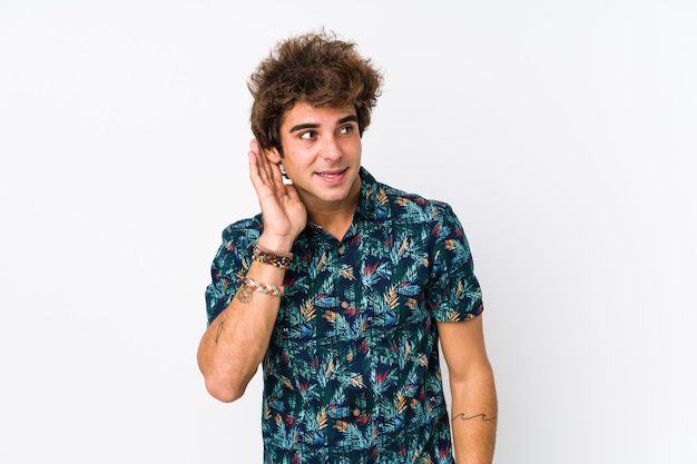 Hombre caucásico joven que llevaba una camiseta de flores aislada tratando de escuchar un chisme.