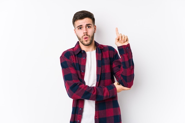 Hombre caucásico joven que presenta en una pared blanca aislada que tiene una gran idea, concepto de creatividad.