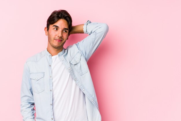 Hombre caucásico joven que presenta en una pared rosada aislada tocando la parte posterior de la cabeza, pensando y tomando una decisión.