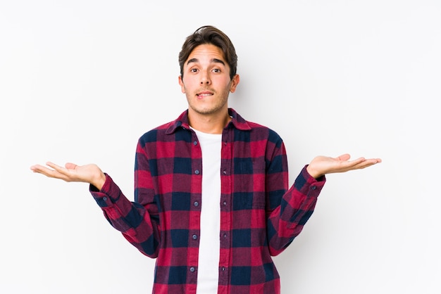 El hombre caucásico joven que presentaba en una pared rosada aisló los hombros de encogimiento confundidos y dudosos para sostener un espacio de la copia.