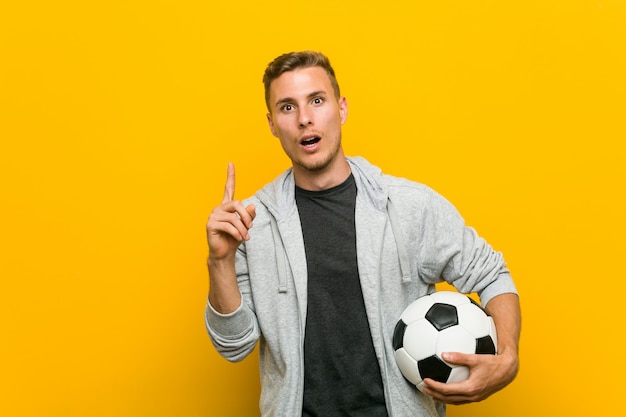 Hombre caucásico joven que sostiene un balón de fútbol que tiene una gran idea, concepto de creatividad.