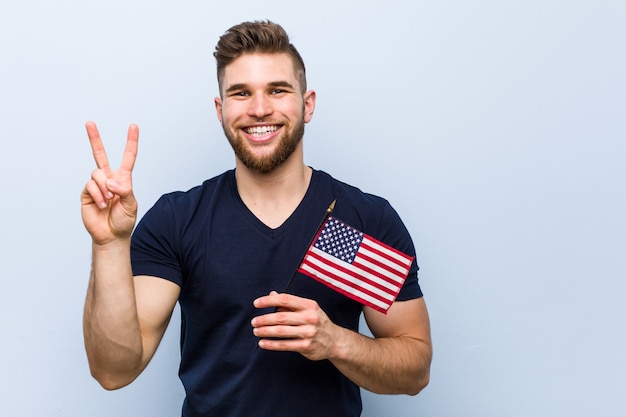 Foto hombre caucásico joven que sostiene una bandera de estados unidos que muestra el número dos con los dedos.