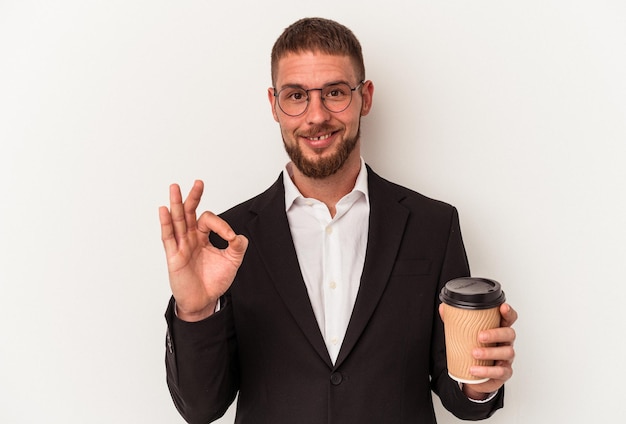 Hombre caucásico joven que sostiene el café para llevar aislado en el fondo blanco alegre y confiado que muestra el gesto aceptable.