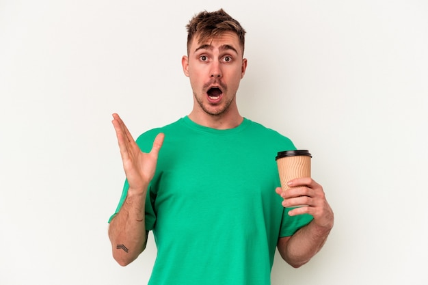 Hombre caucásico joven que sostiene un café para llevar aislado en el fondo blanco sorprendido y consternado.