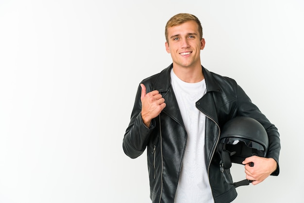 Hombre caucásico joven que sostiene un casco de moto aislado sonriendo y levantando el pulgar hacia arriba