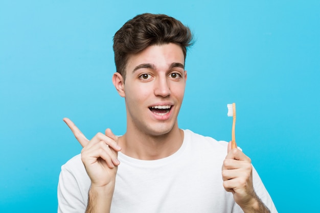 Hombre caucásico joven que sostiene un cepillo de dientes Joven mujer India vistiendo un pijama y máscara para dormir aislado sosteniendo una almohada