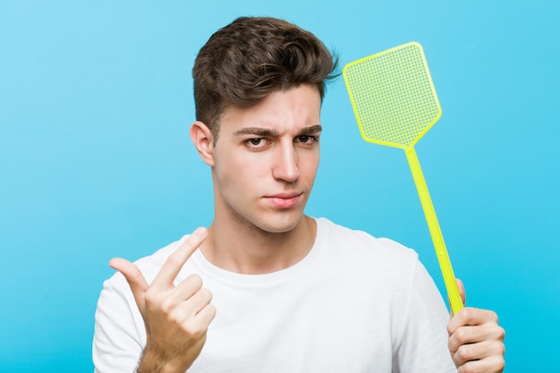 El hombre caucásico joven que sostiene un matamoscas que señala con el dedo a usted como invitando se acerca.