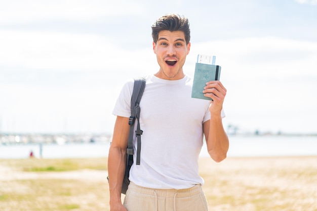 Hombre caucásico joven que sostiene un pasaporte al aire libre con sorpresa y expresión facial conmocionada