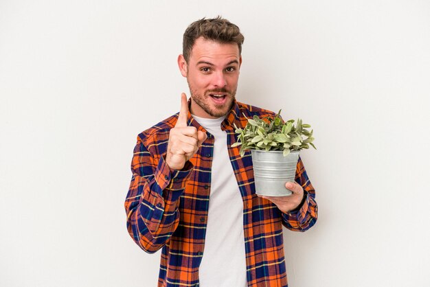 Hombre caucásico joven que sostiene una planta aislada en el fondo blanco que tiene una idea, un concepto de inspiración.