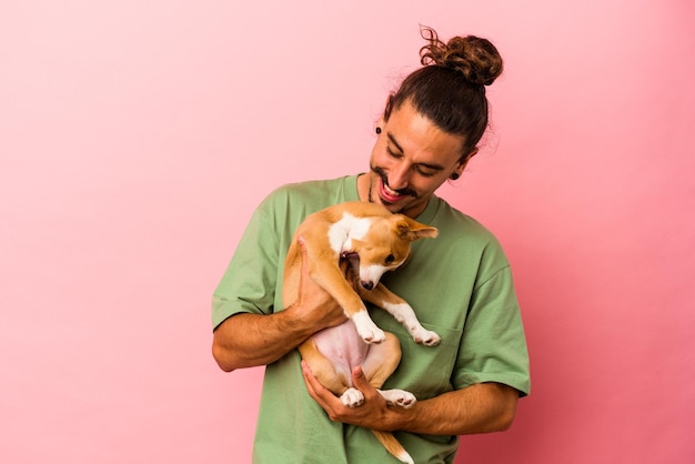 Foto hombre caucásico joven que sostiene su cachorro aislado sobre fondo rosa