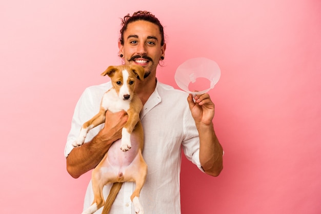 Hombre caucásico joven que sostiene a su cachorro y collar de protección aislado sobre fondo rosa