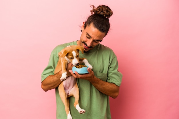 Hombre caucásico joven que sostiene su cachorro y su comida aislado sobre fondo rosa