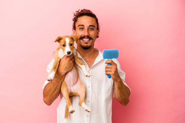 Hombre caucásico joven que sostiene su cepillo del perrito y del perro aislado en fondo rosado