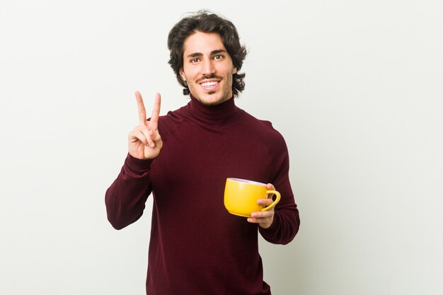 Hombre caucásico joven que sostiene una taza de café que muestra el número dos con los dedos.