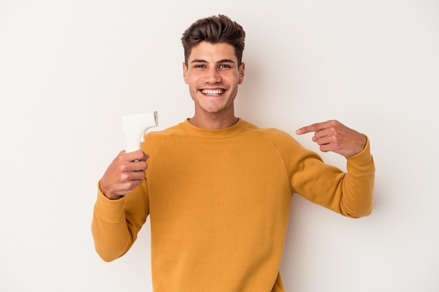 Hombre caucásico joven que sostiene el termómetro aislado en la persona del fondo blanco que señala con la mano a un espacio de la copia de la camisa, orgulloso y confiado