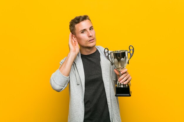 Hombre caucásico joven que sostiene un trofeo tratando de escuchar un chisme.