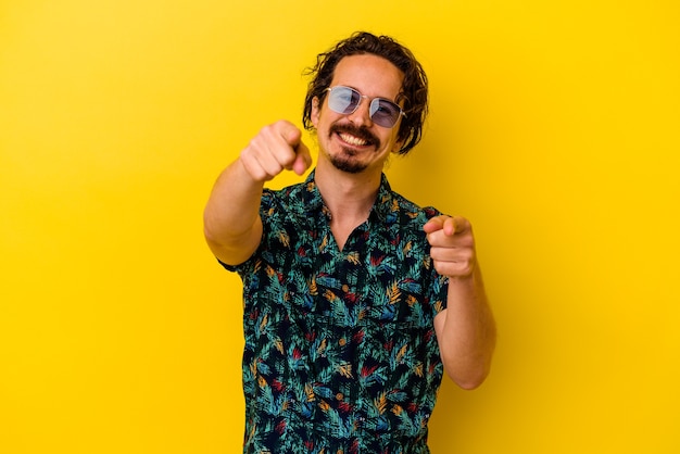 Hombre caucásico joven con ropa de verano aislado en amarillo alegre sonrisas apuntando al frente.