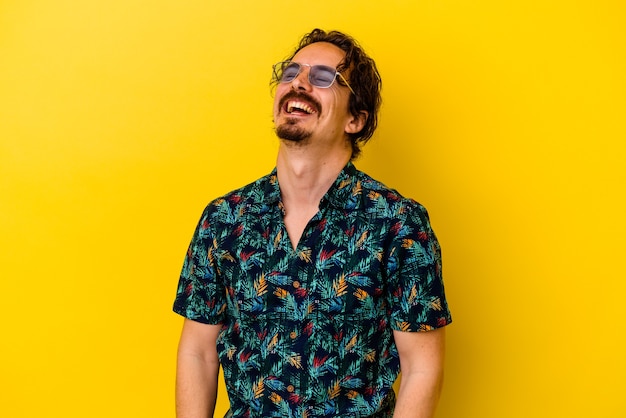 Hombre caucásico joven con ropa de verano aislado en la pared amarilla riendo relajado y feliz, cuello estirado mostrando los dientes.