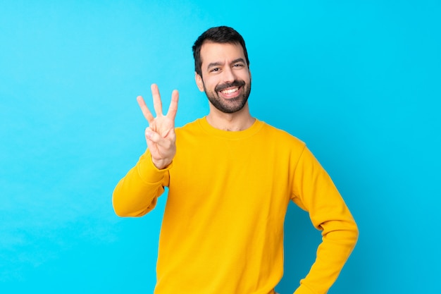 Hombre caucásico joven sobre la pared azul aislada feliz y contando tres con los dedos