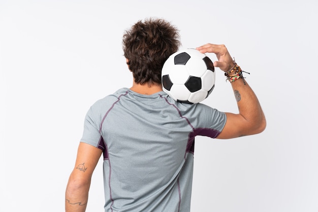 Hombre caucásico joven sobre la pared blanca aislada con balón de fútbol