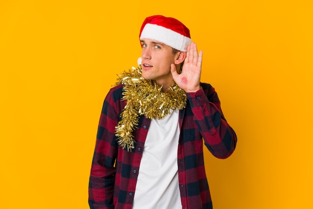 Hombre caucásico joven con sombrero de navidad sosteniendo un presente aislado en la pared amarilla persona apuntando con la mano a un espacio de copia de camisa, orgulloso y seguro