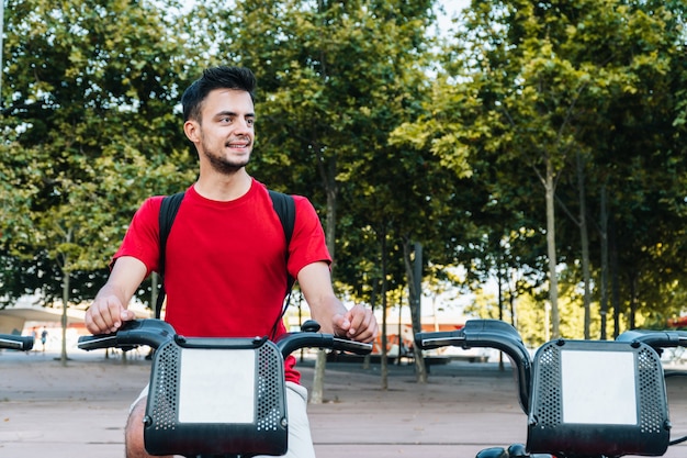 Hombre caucásico joven sonriendo mientras está sentado en una bicicleta alquilada