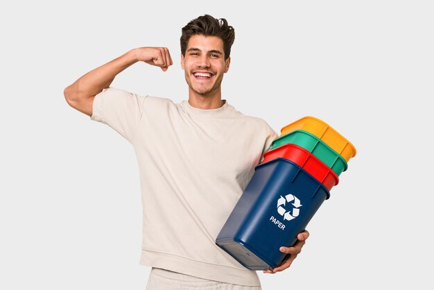 Hombre caucásico joven sosteniendo contenedores de reciclaje aislado sobre fondo blanco.