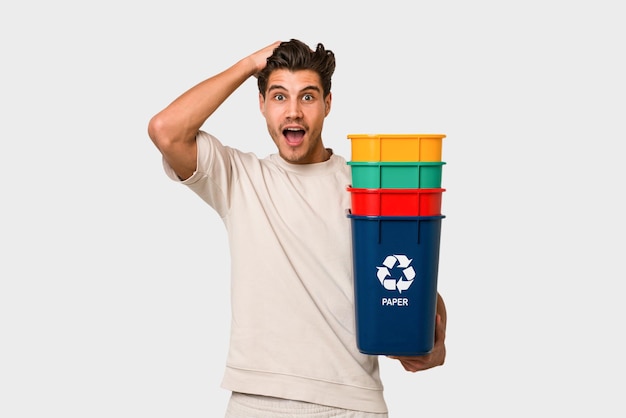 Foto hombre caucásico joven sosteniendo contenedores de reciclaje aislado sobre fondo blanco.