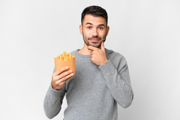 Foto hombre caucásico joven sosteniendo papas fritas sobre fondo blanco aislado pensando