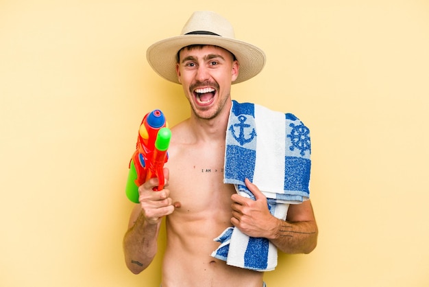 Foto hombre caucásico joven sosteniendo pistola de agua aislado sobre fondo amarillo