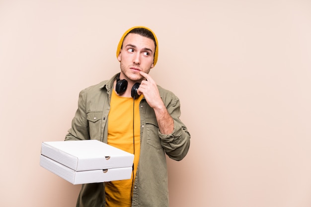 Hombre caucásico joven sosteniendo pizzas relajado pensando en algo mirando un espacio de copia.