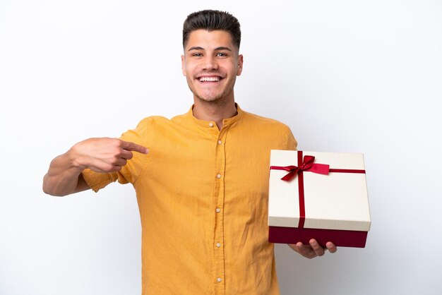 Hombre caucásico joven sosteniendo un regalo aislado sobre fondo blanco con expresión facial sorpresa