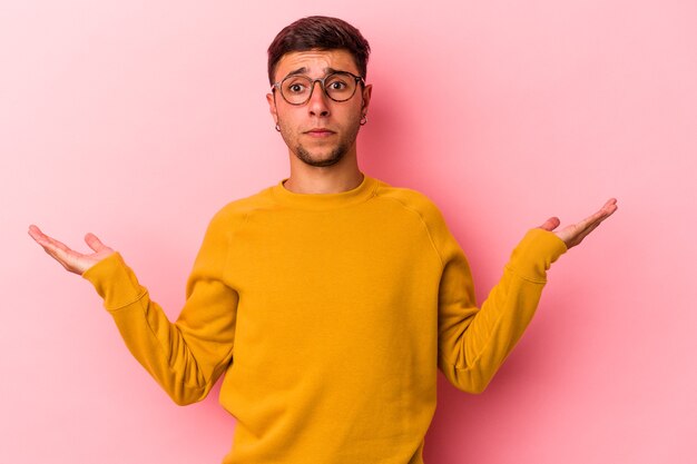 Hombre caucásico joven con tatuajes aislados sobre fondo amarillo confundido y dudoso encogiéndose de hombros para mantener un espacio de copia.