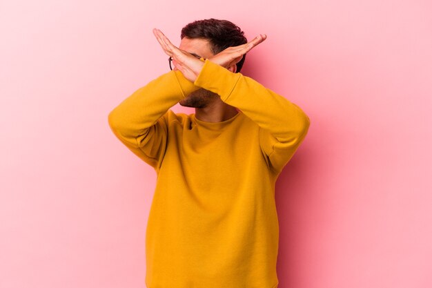 Hombre caucásico joven con tatuajes aislados sobre fondo amarillo manteniendo dos brazos cruzados, concepto de negación.