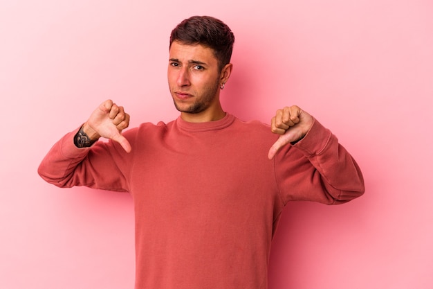 Hombre caucásico joven con tatuajes aislados sobre fondo amarillo mostrando el pulgar hacia abajo, concepto de decepción.