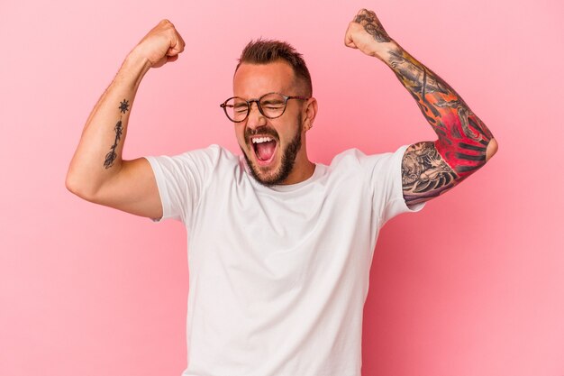 Hombre caucásico joven con tatuajes aislados sobre fondo rosa levantando el puño después de una victoria, concepto ganador.